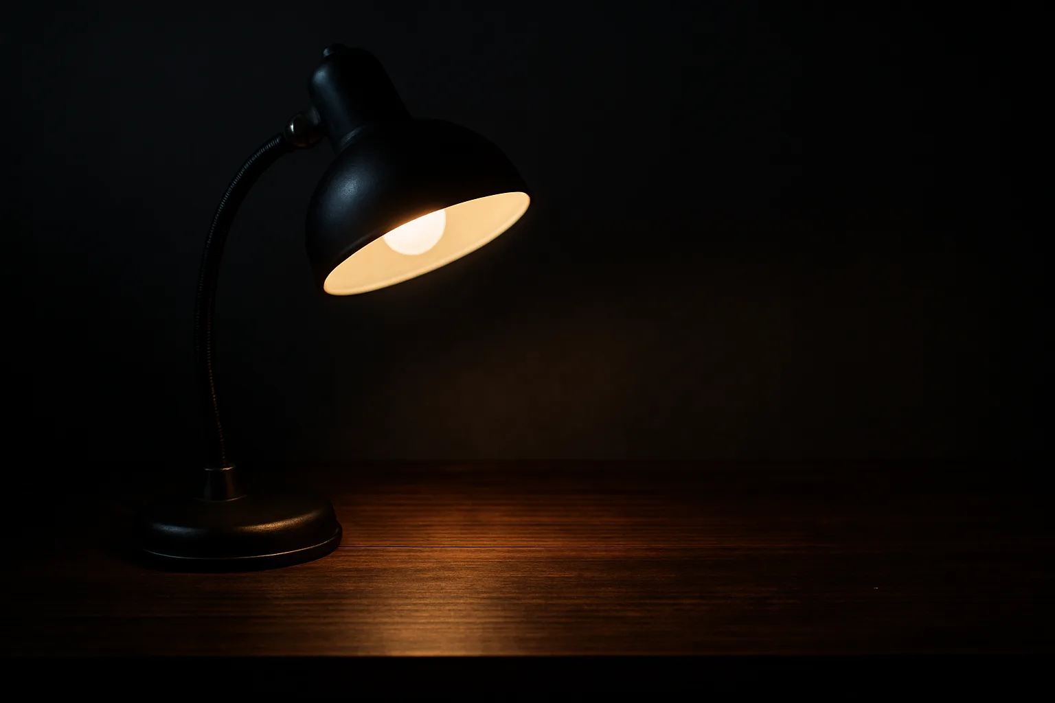 暗い部屋でデスクライトの光が手元だけを照らしている夜のデスク（AI生成イメージ）